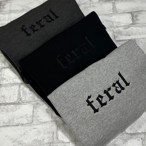 May include: Three gray, black, and dark gray sweatshirts with the word "feral" embroidered in black on each.