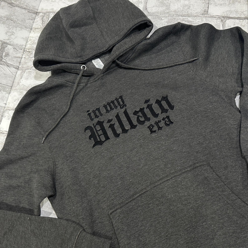 May include: A dark gray hooded sweatshirt with the text "in my Villain era" printed in black on the front.