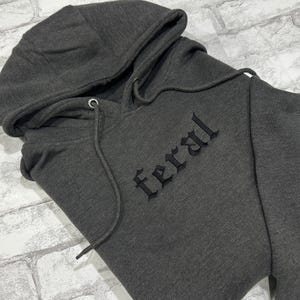 May include: A dark gray hooded sweatshirt with the word "feral" embroidered in black on the front.