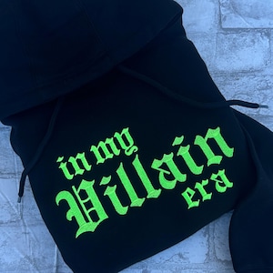 May include: Black hooded sweatshirt with the text "in my Villain era" embroidered in neon green.
