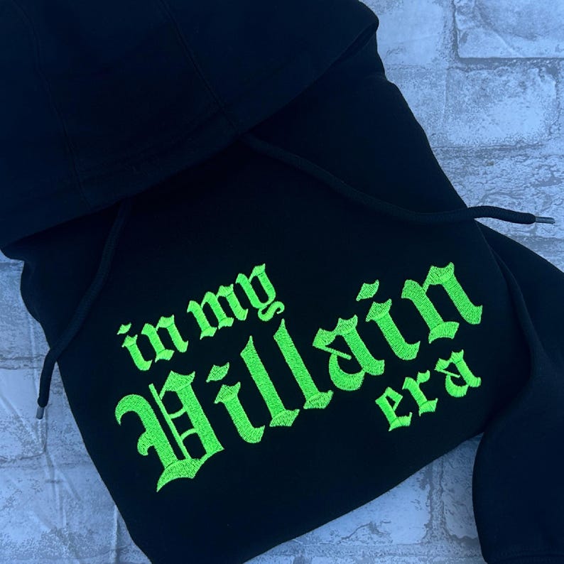May include: Black hooded sweatshirt with the text "in my Villain era" embroidered in neon green.