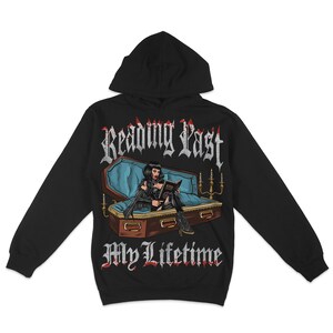 May include: Black hooded sweatshirt with a graphic print of a woman in a coffin reading a book. The text "Reading Past My Lifetime" is printed in white on the front of the sweatshirt.