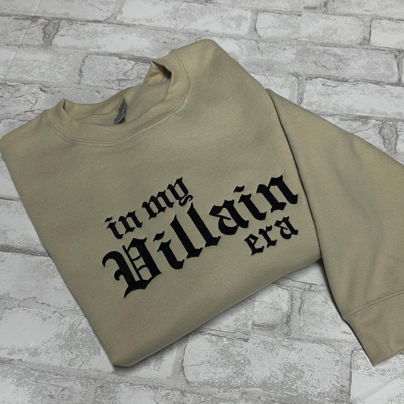 May include: A beige sweatshirt with black embroidered text that reads "in my Villain era".