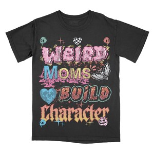 May include: Black t-shirt with the text "Weird Moms Build Character" in a colorful, distressed font. The design includes skulls, hearts, and a moth graphic, creating a vintage, edgy aesthetic. The shirt is a crew neck and has short sleeves.
