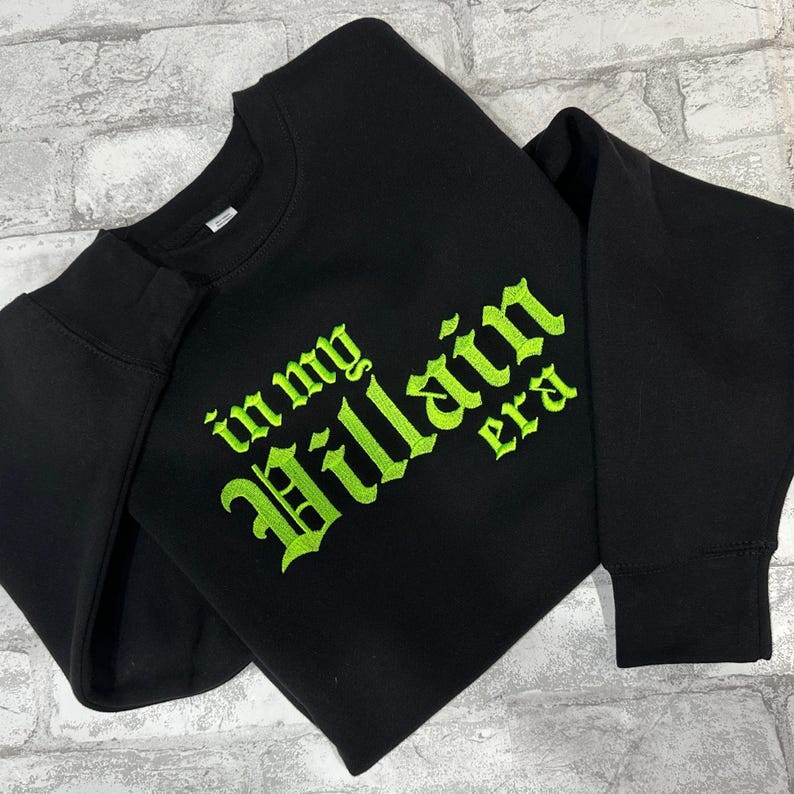May include: Black sweatshirt with a green embroidered design that says "in my Villain Era".
