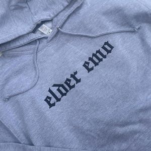 May include: A gray hooded sweatshirt with the text "elder emo" printed in black gothic lettering.
