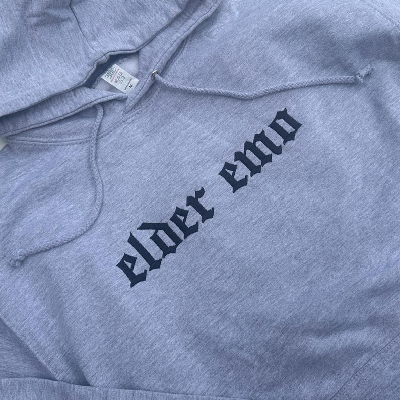 May include: A gray hooded sweatshirt with the text "elder emo" printed in black gothic lettering.