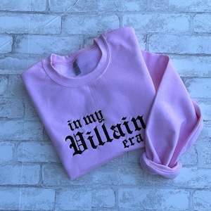 May include: Pink sweatshirt with black text that reads "in my Villain era".