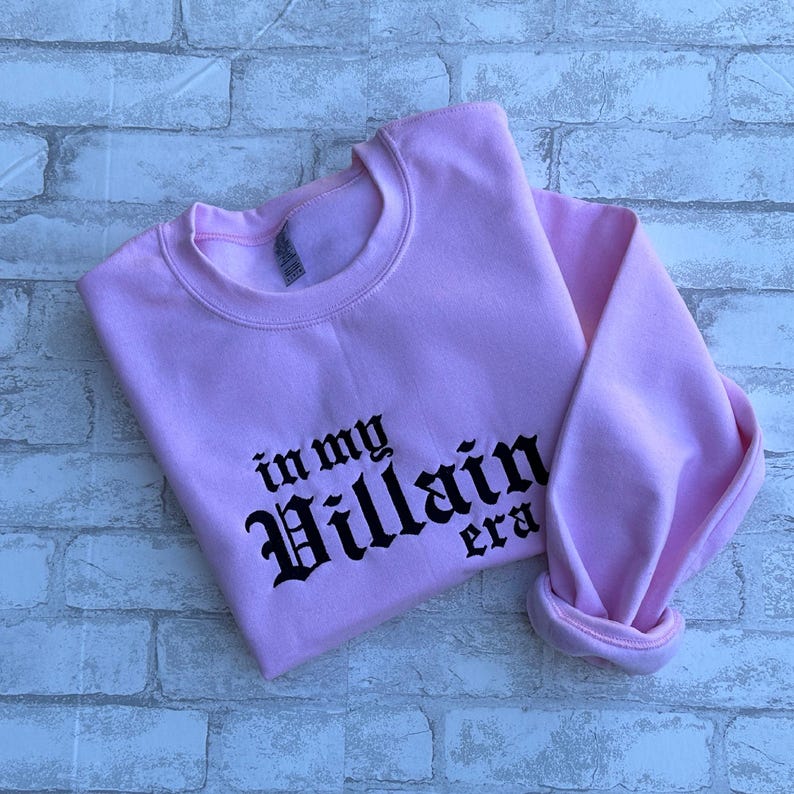 May include: Pink sweatshirt with black text that reads "in my Villain era".