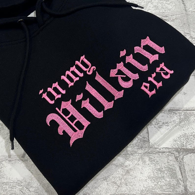May include: Black hoodie with pink embroidered text that reads "in my villain era".