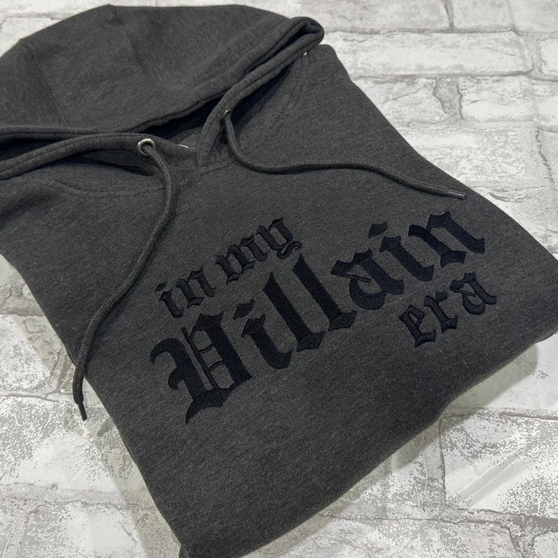 May include: A dark gray hooded sweatshirt with the text "In my Villain era" printed in black.
