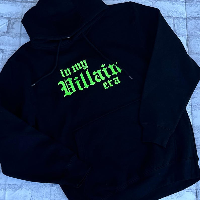 May include: Black hooded sweatshirt with a green embroidered design that says "in my Villain era".