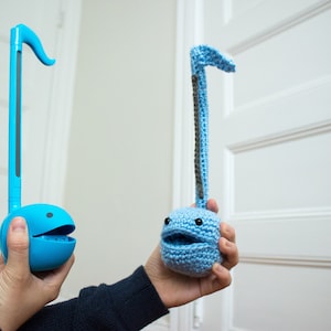 May include: Two blue ukuleles, one is a traditional plastic ukulele and the other is a crocheted ukulele. Both ukuleles have a smiling face.