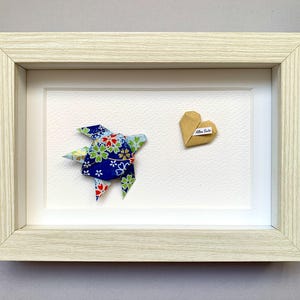 Può includere: Un'opera d'arte origami incorniciata con una tartaruga origami blu, rossa e verde e un cuore origami beige. Il cuore ha una piccola etichetta con testo. La cornice è in legno chiaro.