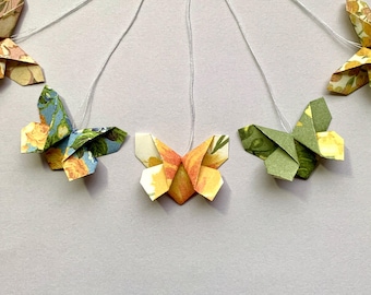 May include: Five origami butterflies hanging from white strings. The butterflies are made of paper with floral patterns in shades of green, blue, yellow, and orange.