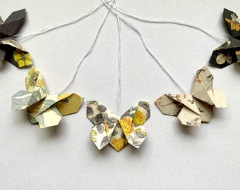 May include: A garland of origami butterflies made from patterned paper. The butterflies are strung together with white thread and feature floral designs in shades of yellow, green, and brown.