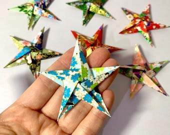 May include: A collection of eight origami stars made from patterned paper. The stars are in various colors and patterns, including blue, green, red, and white. The stars are folded into a five-pointed star shape.