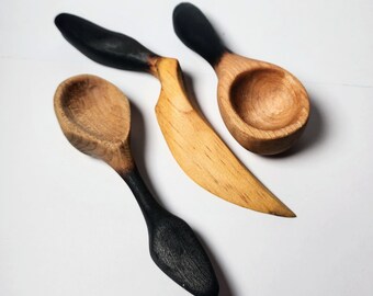 Puede incluir: Tres cucharas de madera con mangos pintados de negro. Dos de las cucharas tienen una forma de cuenco redondeada, mientras que la tercera cuchara tiene una forma de hoja larga y estrecha.