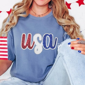 May include: A blue t-shirt with a red, white and blue sequined "USA" graphic.