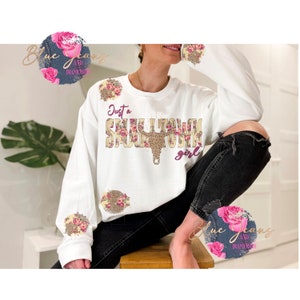 May include: White sweatshirt with the text "Just a Small Town Girl" in pink and brown lettering with floral and leopard print accents.