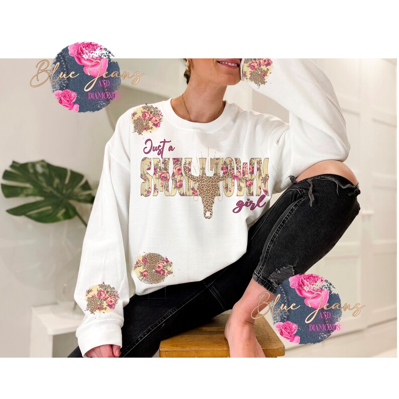 May include: White sweatshirt with the text "Just a Small Town Girl" in pink and brown lettering with floral and leopard print accents.