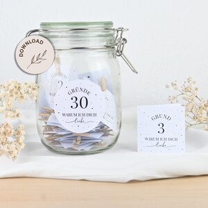 May include: A glass jar filled with white cards with black text. The cards have the text "Gr&uuml;nde 30 Warum ich dich liebe" and "Grund 3 Warum ich dich liebe".