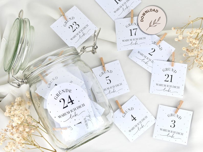 May include: A glass jar filled with white cards with black text. Each card has a number and the text "Grund" and "Warum ich dich liebe". The cards are held together with clothespins. There are also several cards scattered around the jar.