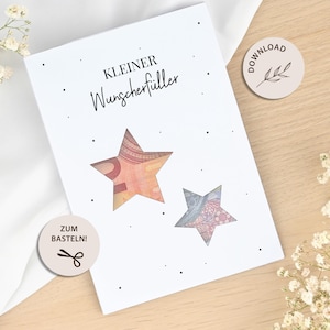 Pode incluir: Um cartão branco com o texto alemão "Kleiner Wunschfüller" e dois recortes em forma de estrela. Um recorte revela uma parte de uma nota de euro, e o outro mostra um desenho padronizado. Pequenos pontos pretos estão espalhados em torno do texto.