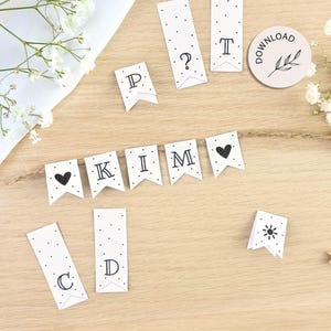 Könnte beinhalten: Weiße Papierbanner-Flaggen mit schwarzen Tupfen und Buchstaben, die "KIM" buchstabieren. Zusätzliche Flaggen mit Buchstaben, einem Fragezeichen und einer Sonnengrafik. Ein runder Aufkleber mit dem Wort "download" und einem Blattdesign.