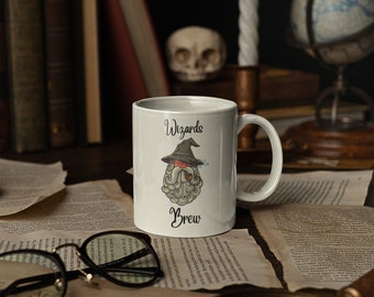May include: White ceramic mug with the words "Wizards Brew" and a cartoon wizard illustration. The wizard has a long white beard, a black hat, and is smoking a pipe. The mug is on a table with books and a globe.