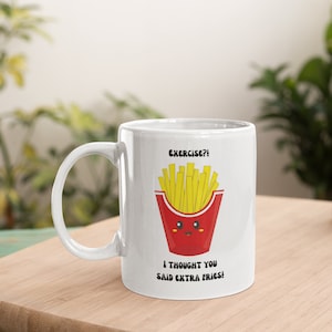 Puede incluir: Taza de cerámica blanca con un diseño humorístico. La taza presenta una imagen de dibujos animados de un recipiente de patatas fritas rojo lleno de patatas fritas amarillas. El texto encima de las patatas fritas dice "Exercise?!" y debajo "I thought you said extra fries!"