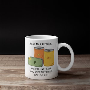 May include: White ceramic mug with the text "YES I AM A PREPPER... NO, I WILL NOT SAVE YOU WHEN THE WORLD GOES TO SHIT!". The mug features illustrations of canned goods and a green rectangle.