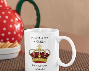 Op de afbeelding: Witte keramische mok met de tekst "IM NOT JUST A QUEEN IM A DRAMA QUEEN!" en een gedetailleerde illustratie van een rode en gouden kroon. De mok heeft een groot oor. De achtergrond is neutraal.
