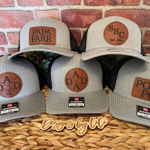 May include: Five gray and black baseball caps with brown leather patches. The patches have different text on them, including "Papa Farr", "SBC Est. 1984", "A Dad A", and "Pop Pop".