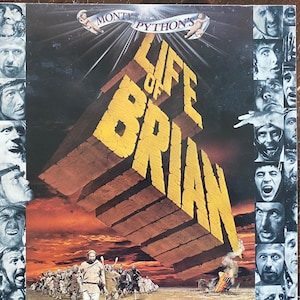 May include: A vintage vinyl record cover for the Monty Python's Life of Brian movie. The cover features a large, yellow, 3D title with a desert scene in the background. The cover is surrounded by a border of faces.
