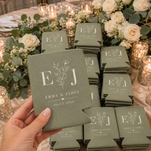 May include: A sage green foam can cooler featuring a white printed design with the initials E and J, a floral illustration, the names Emma & James, and the date 06.22.2026. The item has a rectangular body with a notched base for a beverage can.