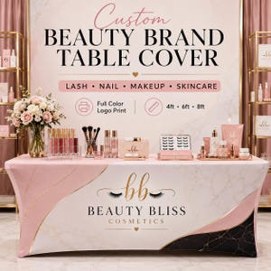 May include: A custom beauty brand table cover with the text "BEAUTY BLISS COSMETICS". The cover is pink and white with gold and black accents. The table is decorated with makeup products, brushes, and flowers.