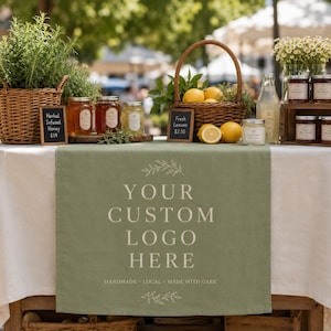 Könnte beinhalten: Ein salbeigrüner Tischläufer mit dem Text YOUR CUSTOM LOGO HERE und HANDMADE LOCAL MADE WITH CARE, präsentiert auf einem Tisch mit Weidenkörben, Honiggläsern, frischen Zitronen und einer klaren Glasflasche mit Flüssigkeit.
