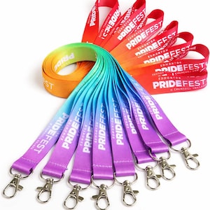 Könnte beinhalten: Eine Auswahl an PrideFest-Lanyards in Regenbogenfarben. Die Lanyards mit silbernen Verschlüssen wechseln von Rot zu Violett. Auf jedem steht "PRIDEFEST EDMONTON". Ideal für Veranstaltungen und Feiern.