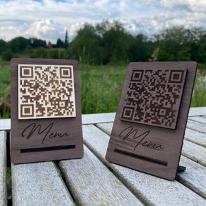 Puede incluir: Dos portamenús de madera con un código QR y la palabra "Menú" grabada en ellos. Los soportes son de madera oscura y tienen una incrustación de madera clara para el código QR.
