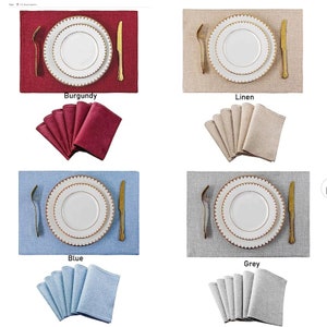 Op de afbeelding: Vier placemats met bijpassende servetten in vier verschillende kleuren: bordeauxrood, linnen, blauw en grijs. Elke placemat heeft een wit bord met een gouden rand en een gouden vork en mes.