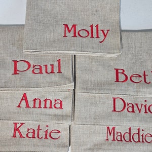 Op de afbeelding: Een set van tien beige linnen placecards met rode geborduurde namen: Molly, Paul, Beth, Anna, David, Katie en Maddie.