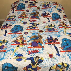 May include: A white twin-sized bed sheet with a colorful X-Men comic book print. The sheet features various X-Men characters, including Wolverine, Cyclops, Gambit, Rogue, and Beast. The characters are depicted in action poses against a blue and white background.