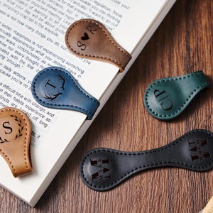 May include: Five different leather book markers with personalised initials and designs. The markers are in brown, blue, green, and black leather.