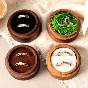 May include: Four wooden ring boxes with velvet interiors. Two boxes have a single ring, one has two rings, and one has a bed of green moss with two rings.