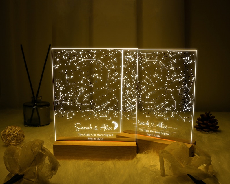 Puede incluir: Dos placas acr&iacute;licas iluminadas con un dise&ntilde;o de constelaci&oacute;n de estrellas. Las placas est&aacute;n sobre bases de madera y tienen el texto "Sarah & Alix The Night Our Stars Aligned May 15 2014" en cada una.