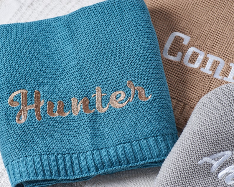 May include: A teal blue knitted baby blanket with the name "Hunter" embroidered in gold thread.