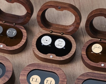May include: Several wooden ring boxes with oval openings are displayed. Each box is open, revealing a pair of cufflinks. The cufflinks are round with various initials and dates. The boxes are made of dark wood and have a hinged lid.