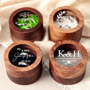 May include: Four wooden ring boxes with clear glass lids. Each box has a different engraved design and date. The designs include floral, initials, and a name.