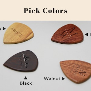 May include: Four guitar picks made of different types of wood. The picks are in the colors oak, red, black, and walnut. Each pick has a different design engraved on it.